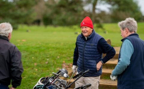 Elderly Man in Red Hat Smiling and Talking to Other Man on Golf Field